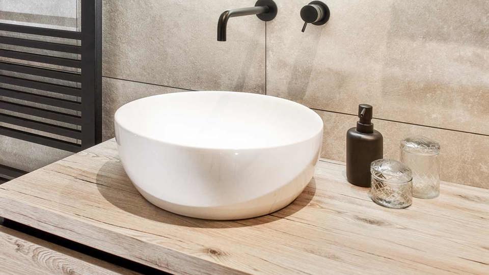 Houten wastafelmeubel met witte waskom en zwarte badkamer kraan