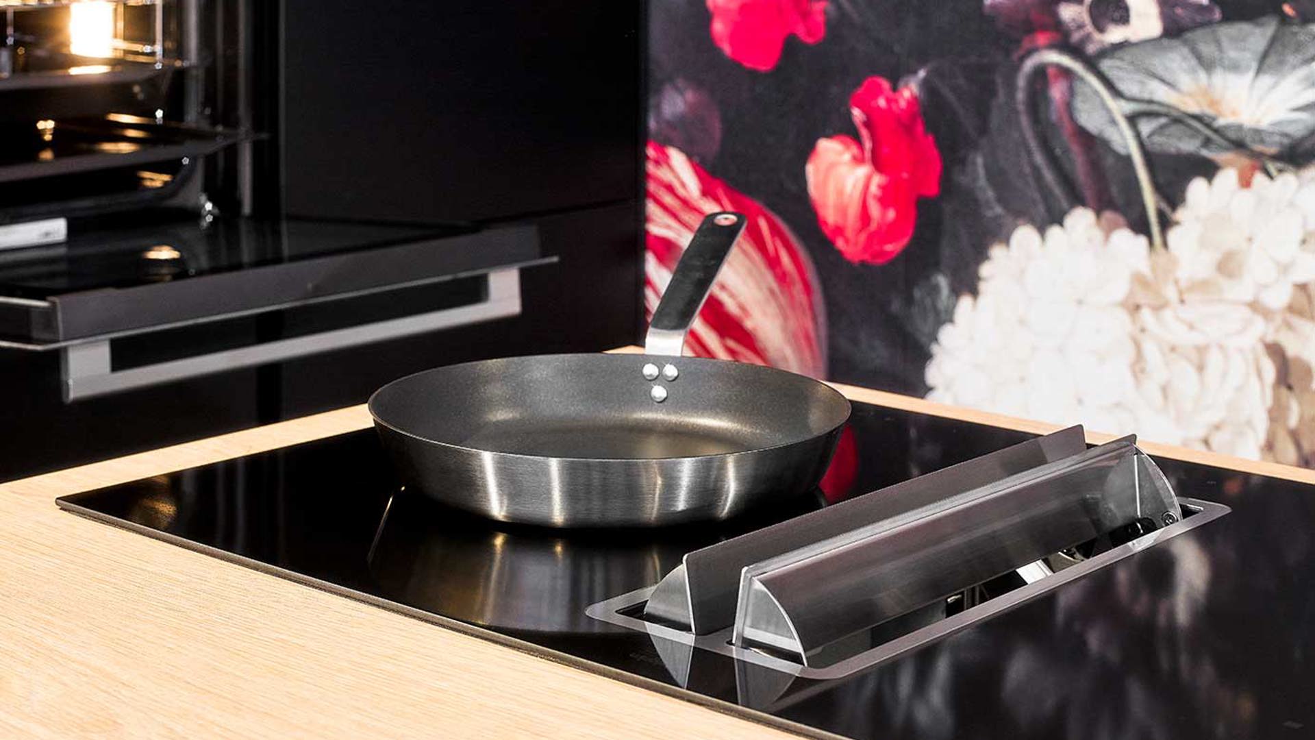 Zwarte eilandkeuken met kastenwand, inductiekookplaat met geïntegreerde afzuiging