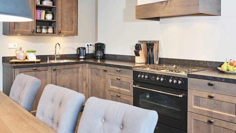Houten hoekkeuken in landelijke stijl met bovenkasten, fornuis en schouw