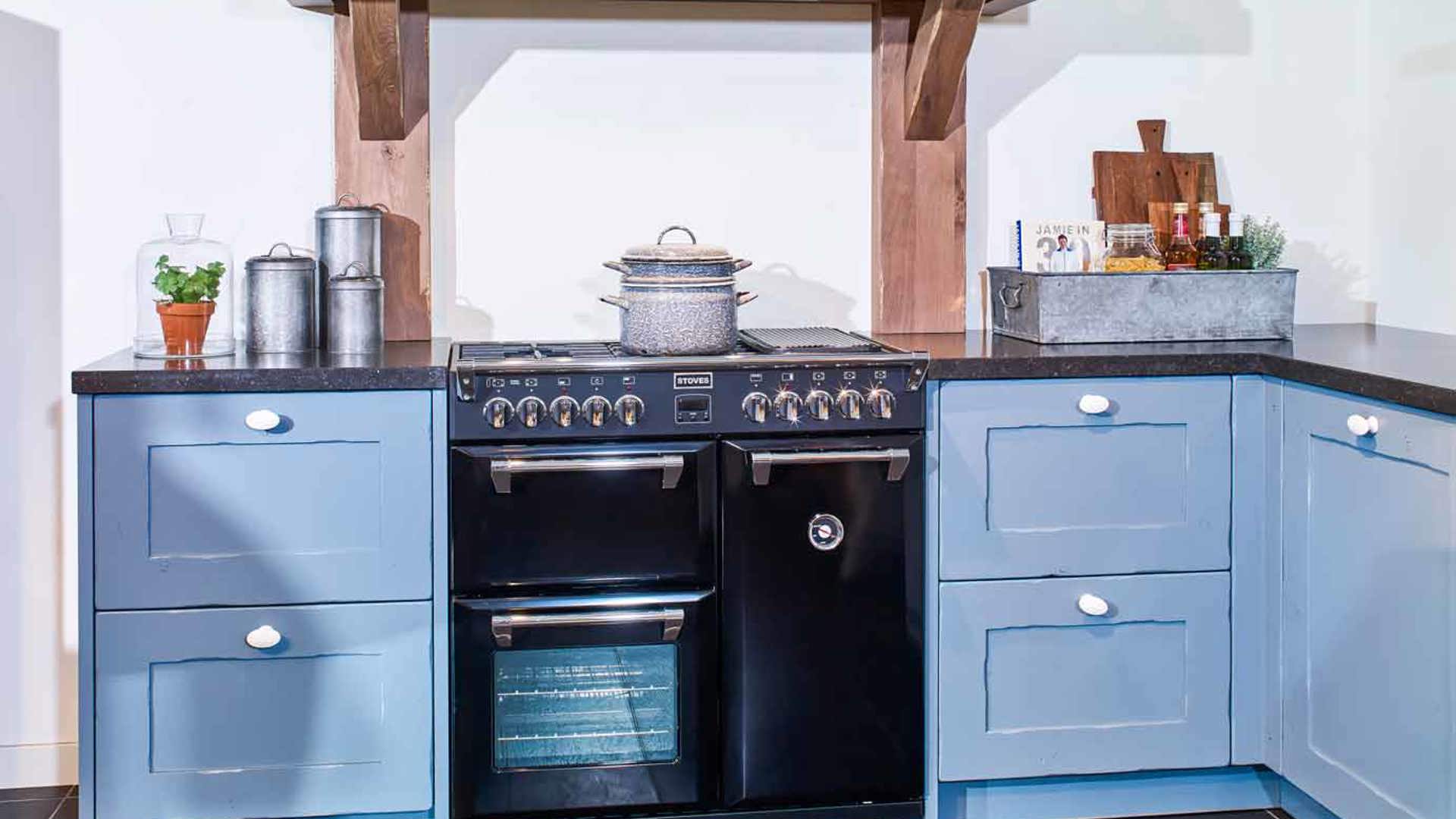 Blauwe landelijke keuken met fornuis en houten balk bij de schouw
