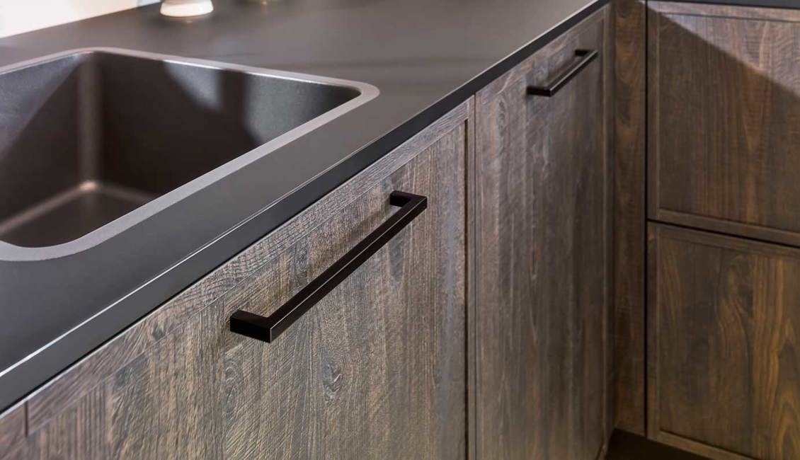 De zwarte handgrepen in deze houtlook keuken combineren mooi met het donkere werkblad